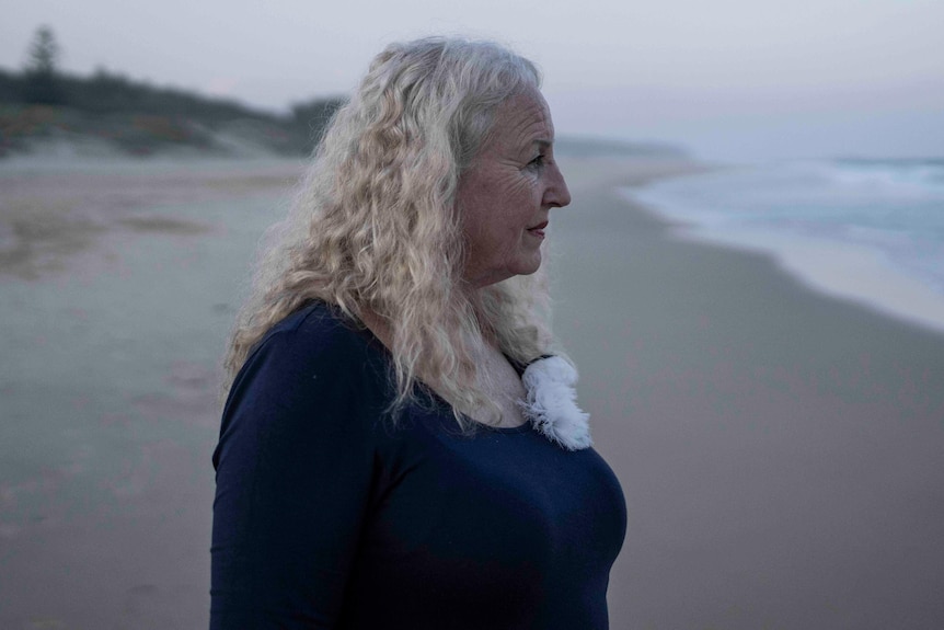 woman with white curly hair looks at beach shoreline at sunset