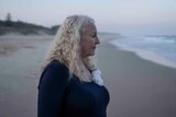 woman with white curly hair looks at beach shoreline at sunset