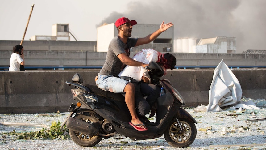 A man rides a motor scooter with an bleeding victim slumped over the handle bars.