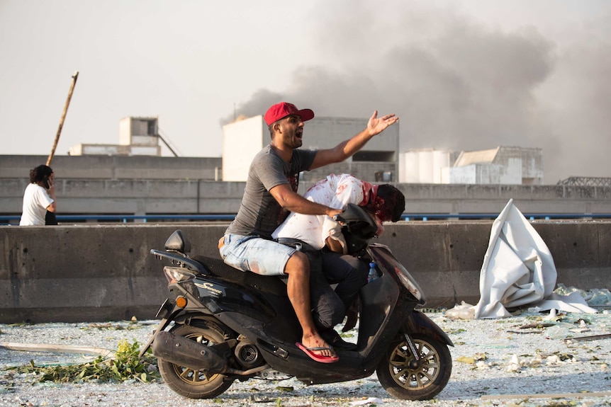 A man rides a motor scooter with an bleeding victim slumped over the handle bars.