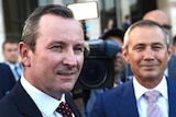 Mark McGowan and Roger Cook stand outside WA Parliament, smiling. In the background is a cameraman.