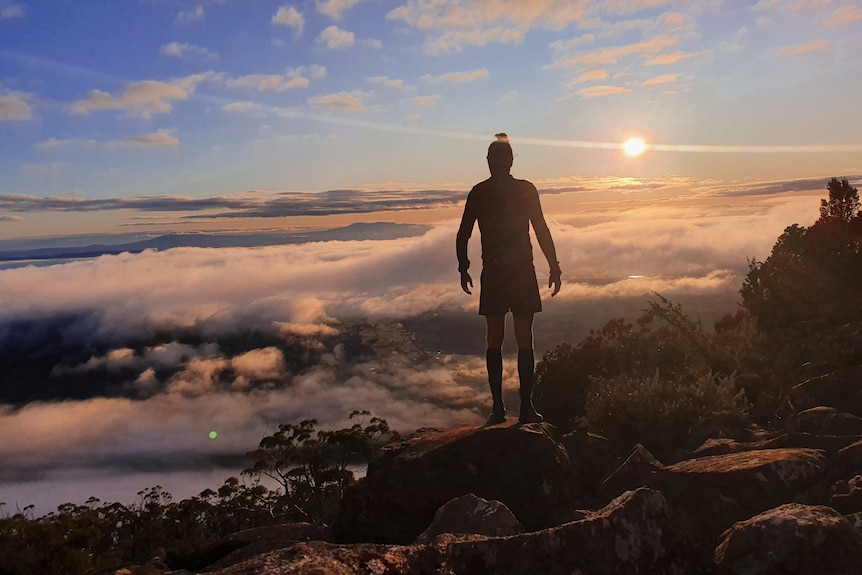 A man on a mountain top silhouetted against a rising or setting sun.