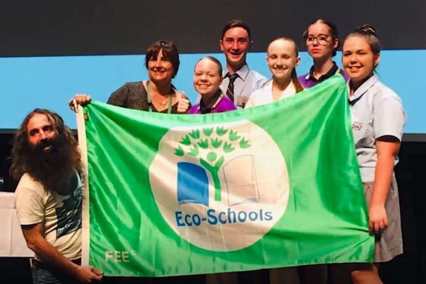 A woman, some school students and Costa from Gardening Australia hold up a banner that says 'Eco schools' at a conference.
