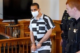 Hadi Matar, 24, center, arrives for an arraignment in cuffs, wearing black and white prison clothes and a mask.
