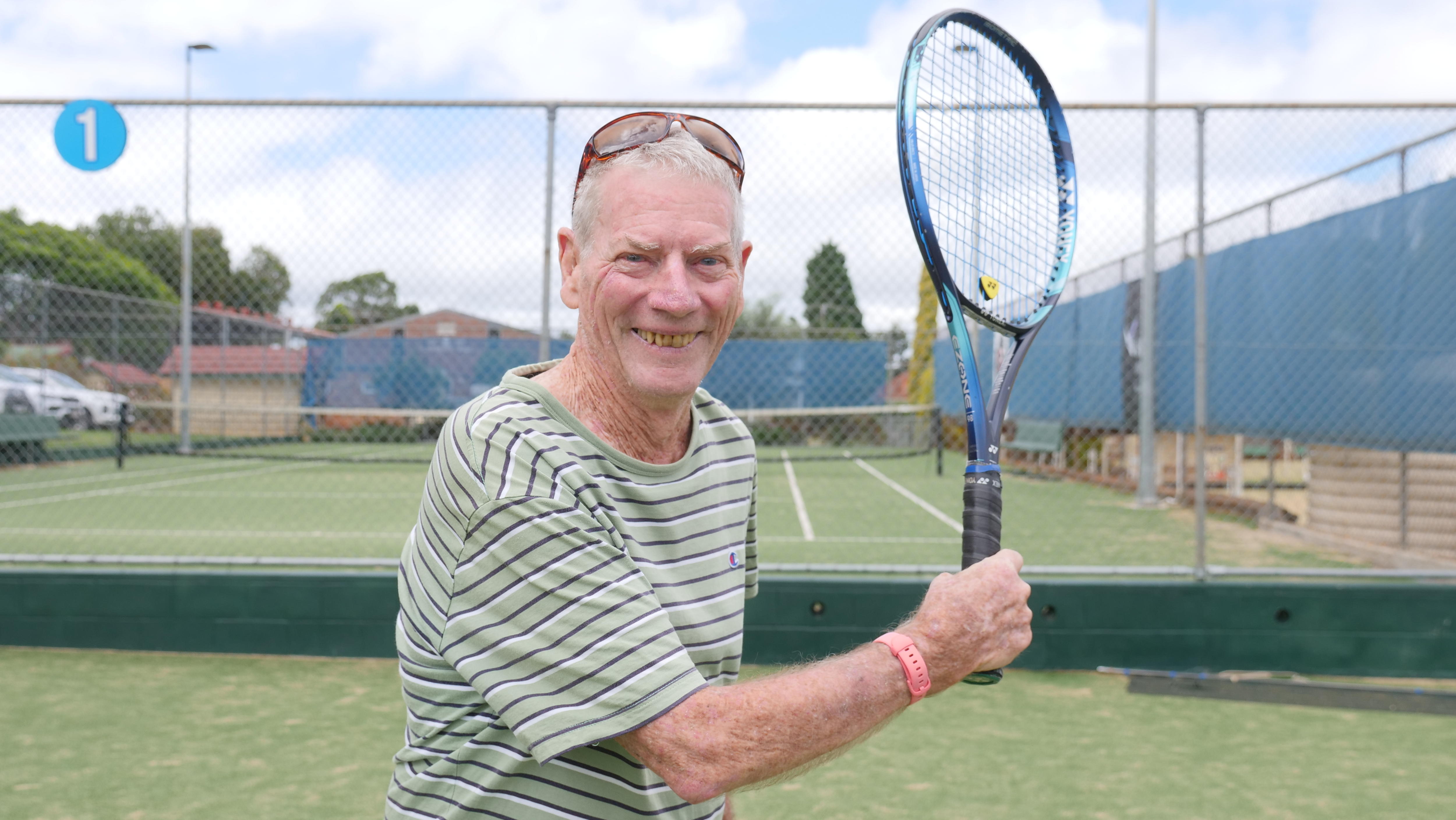 Hombre de unos ochenta años sonriendo y sosteniendo una raqueta de tenis