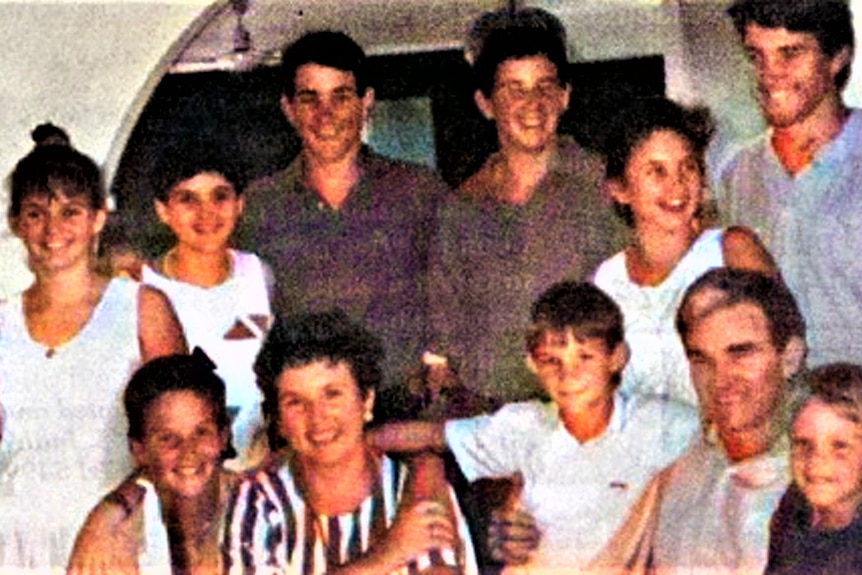 A young family with two parents and nine children pose in a group photo with arms around each other.