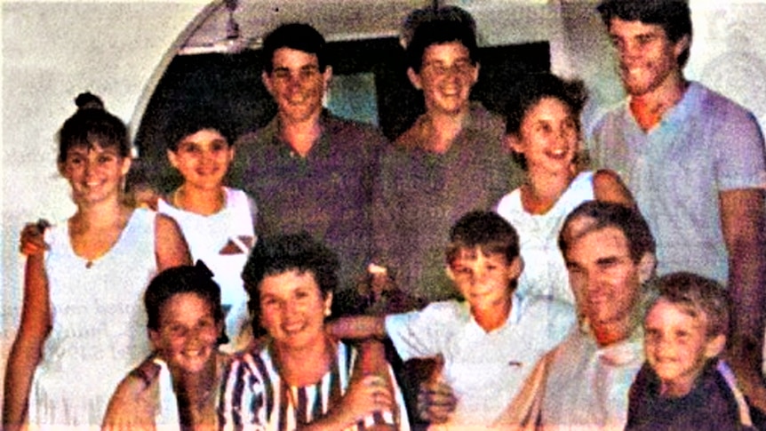A young family with two parents and nine children pose in a group photo with arms around each other.