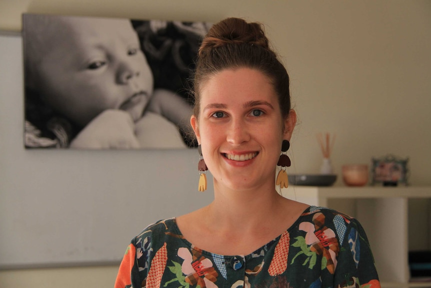 A woman standing in her kinesiology room with a large picture of a baby on the wall.