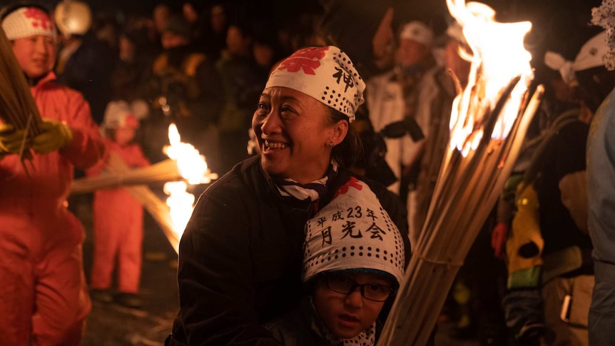 A woman clutches a young child as they hold flaming torches.