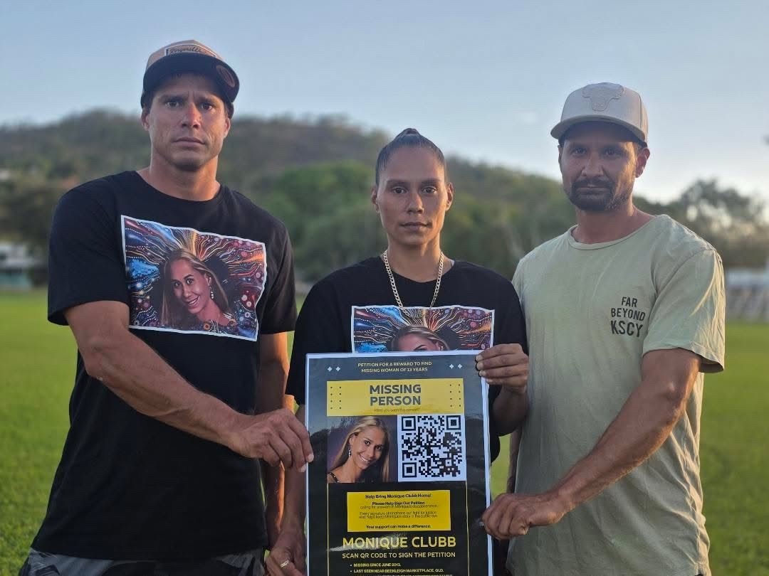 Three siblings wearing matching shirts hold a large black and yellow poster.