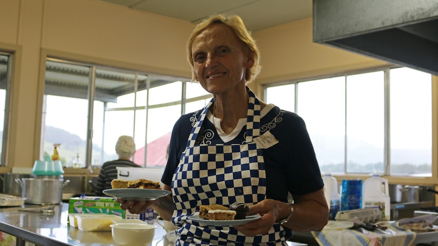 Judy Hopkins in the show kitchen holding two plates of slices and looking towards the camera.