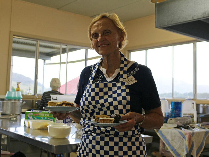 Judy Hopkins in the show kitchen holding two plates of slices and looking towards the camera.