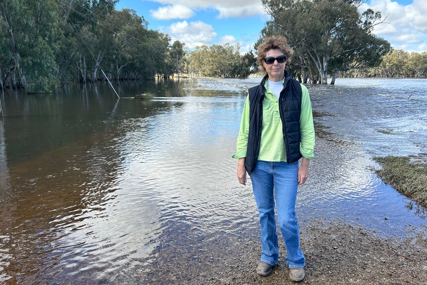 A woman stands next to a flooded road, looking at the camera. 