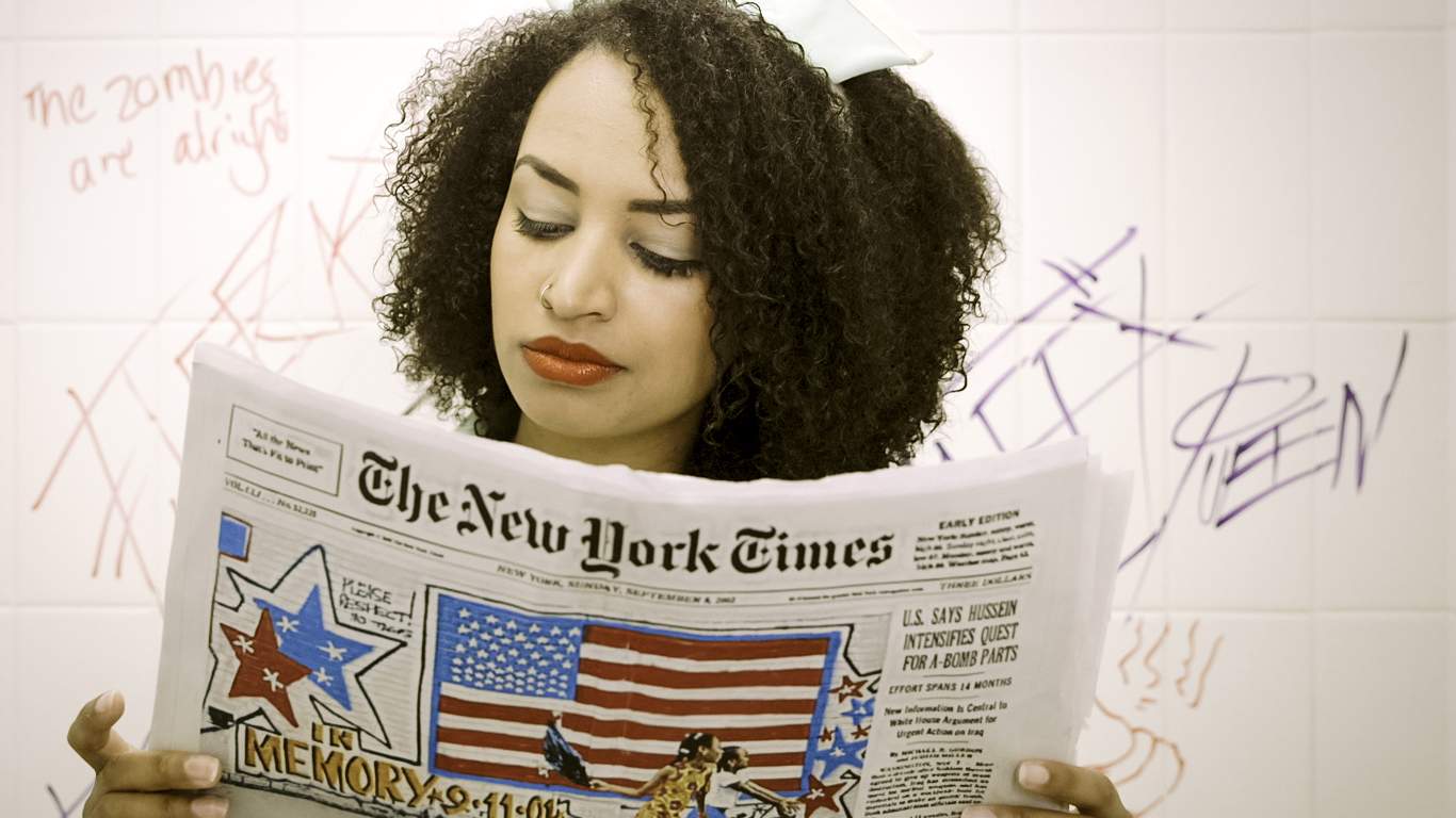 Amelia reads the newspaper wearing a retro waitress costume with Zombie related graffiti in the background.
