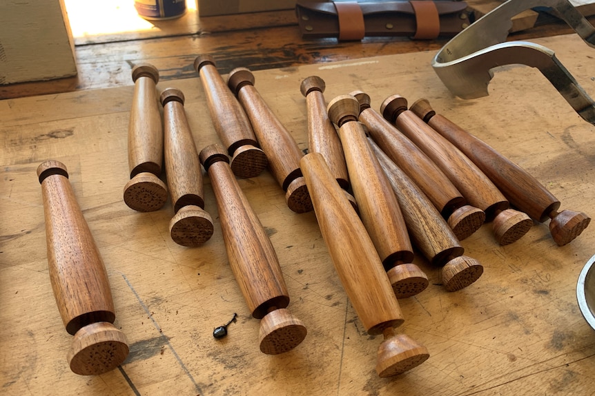 Thirteen wooden tool handles on a bench ready to have metal blades inserted.