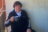 a man sitting on a balcony holding a cup and looking at the camera