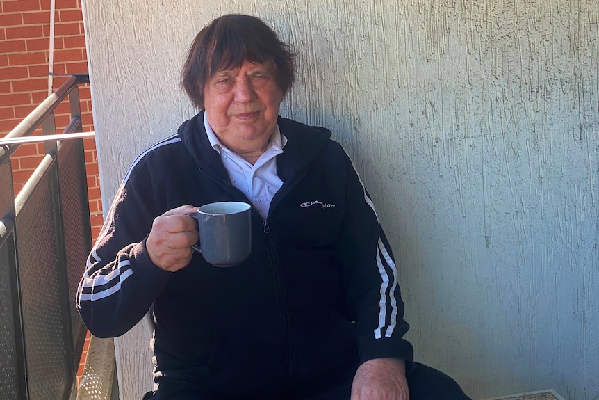 a man sitting on a balcony holding a cup and looking at the camera