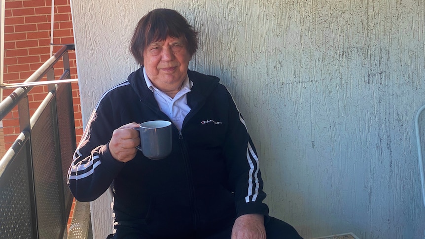 a man sitting on a balcony holding a cup and looking at the camera