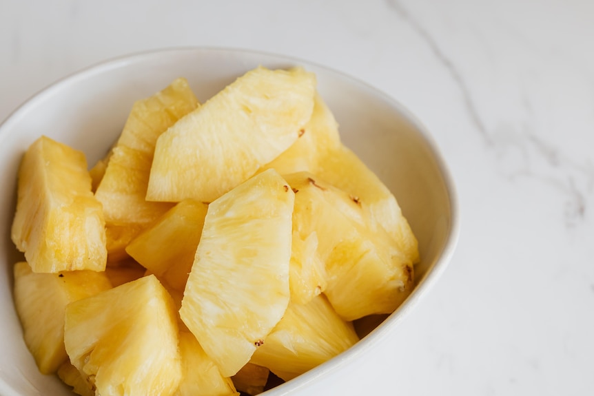 A bowl of fresh pineapple slices, the spiky exterior cut off for easy eating.