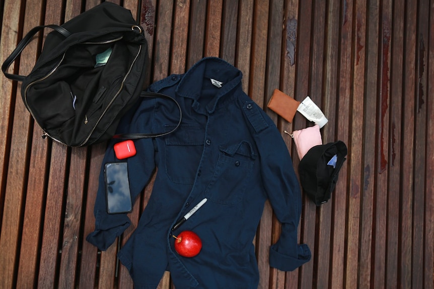 Bird's eye view of a handbag on a wooden bench with items pulled out beside it.