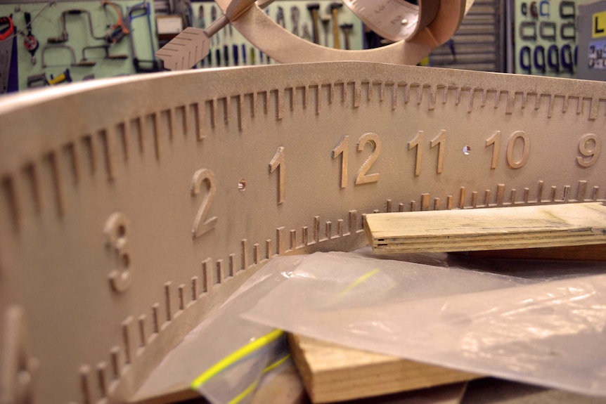 Numbers at carefully spaced intervals are marked along the inside curve of a long piece of bent brass.