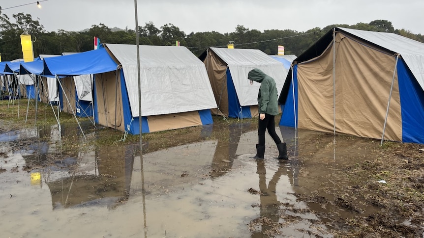 A person walking through mud with tents behind them