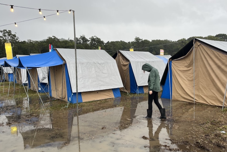 A person walking through mud with tents behind them