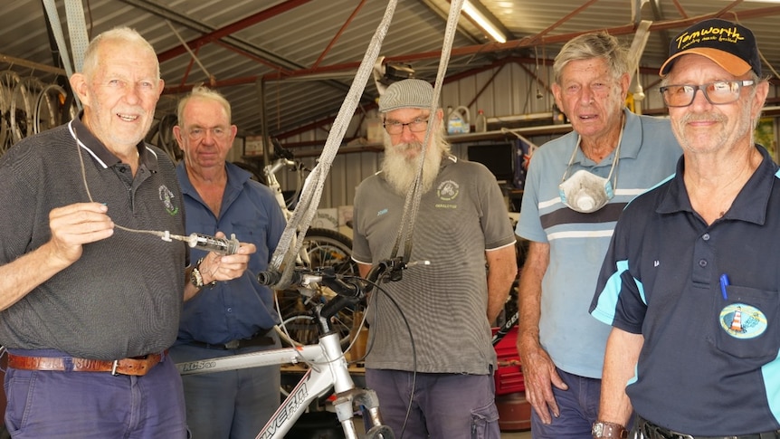 Five men stand next to a bike they're working on.