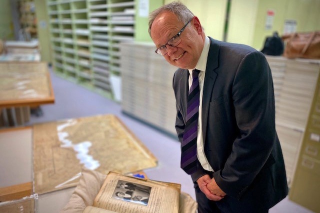 WA Minister for Culture and the Arts David Templeman poses for a photo smiling while standing over historical documents.