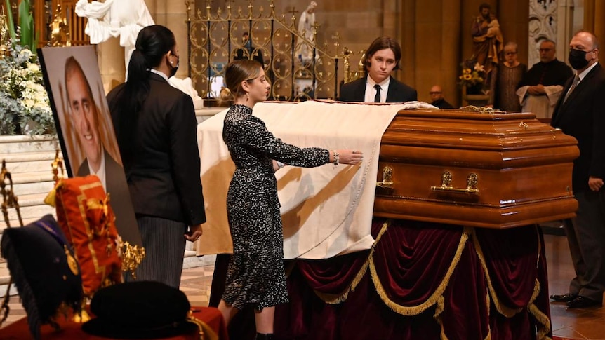 People stand next to a coffin