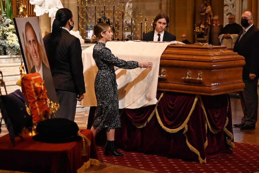 People stand next to a coffin