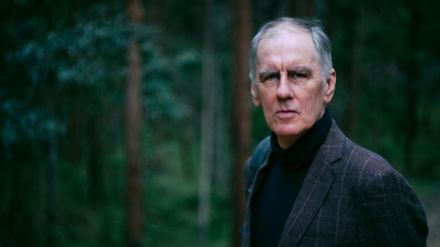 grey-haired man in black top and grey jacket in lush bush