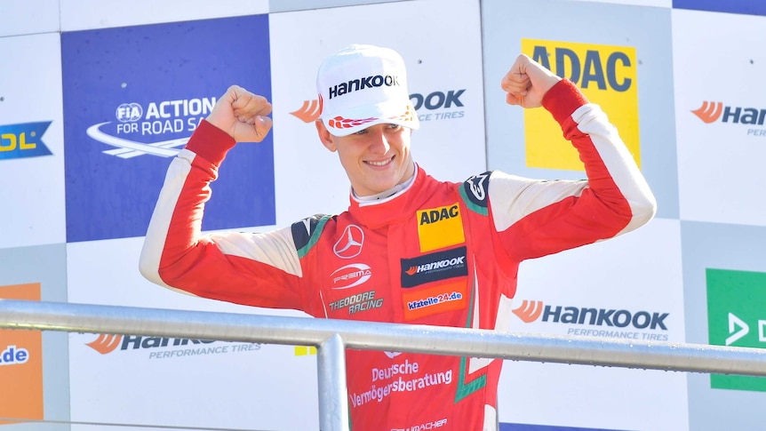 A man in red overalls clenches both fist above his head and smiles.