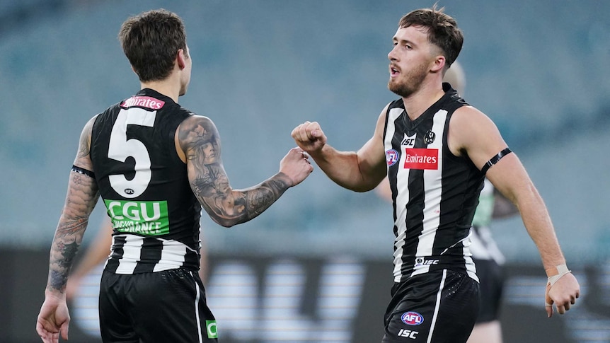 Two Collingwood players celebrate a goal at an empty stadium.