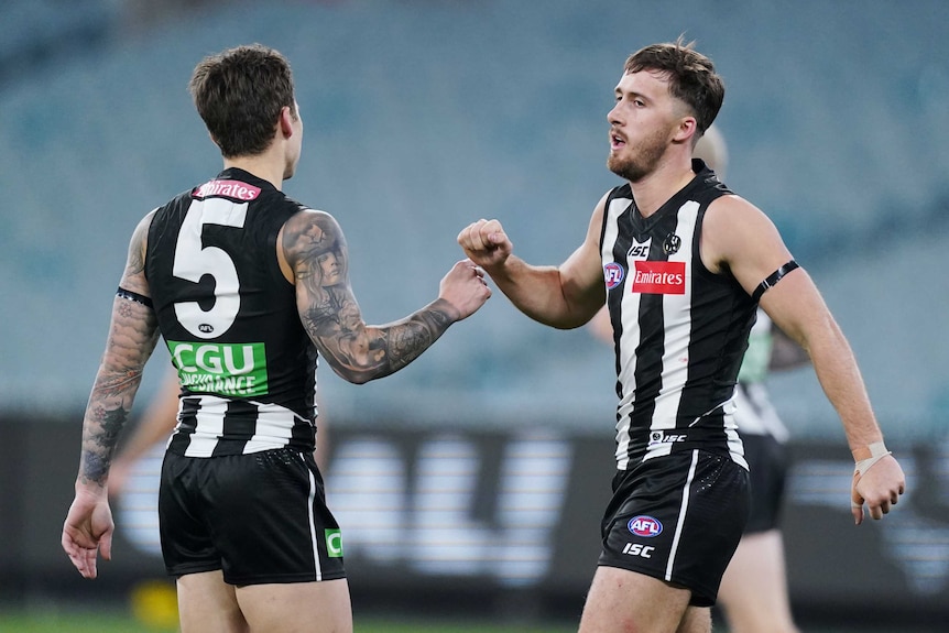 Two Collingwood players celebrate a goal at an empty stadium.