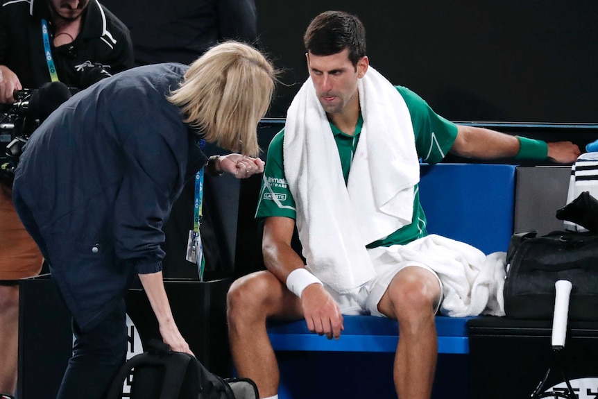 A male tennis player speaks to a medical official on court at the Australian Open