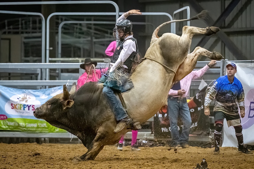 A teenager sits atop a bucking bull in a rodeo arena