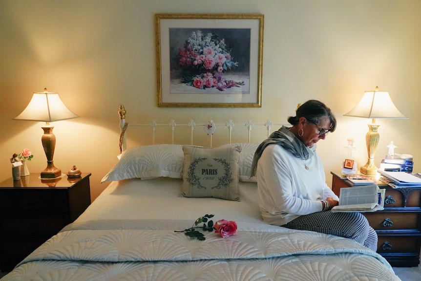 A woman sits on the side of her bed