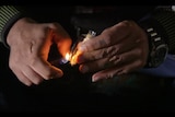 Close shot of hands holding lighter and pack of pills.