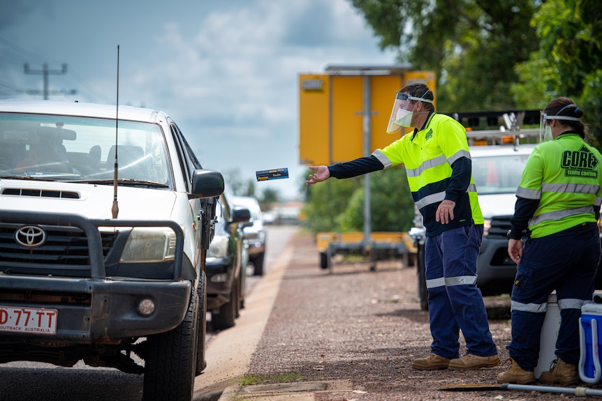 A worker wearing PPE throws an RAT test underarm through a vehicle's passenger window