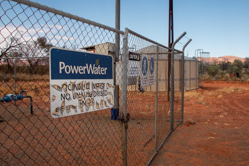 A sign with peeling letters, that reads PowerWater no unauthorised personnel, on a fence in the desert