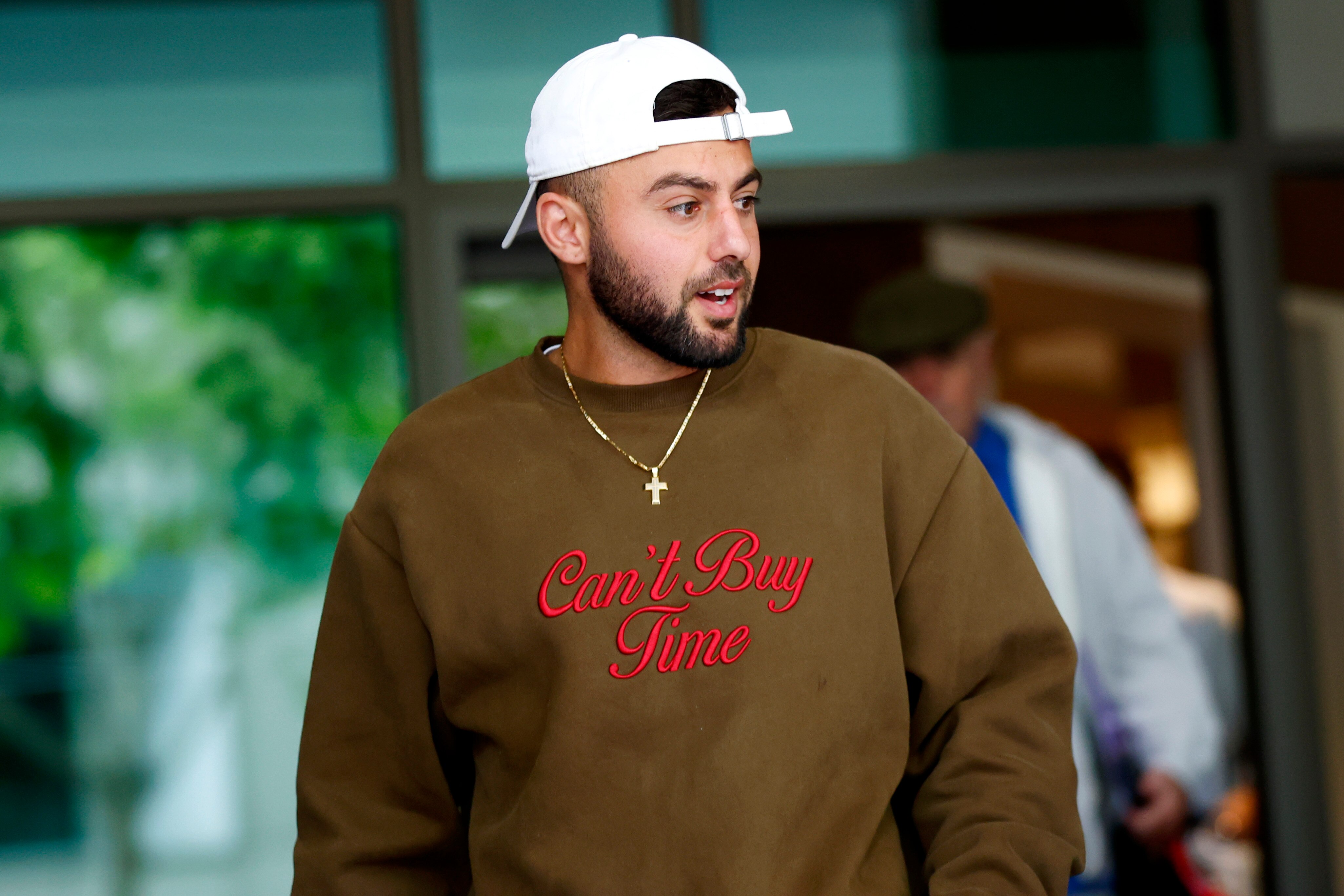 Christian Salem lleva una gorra blanca al revés y un collar con una cruz plateada.