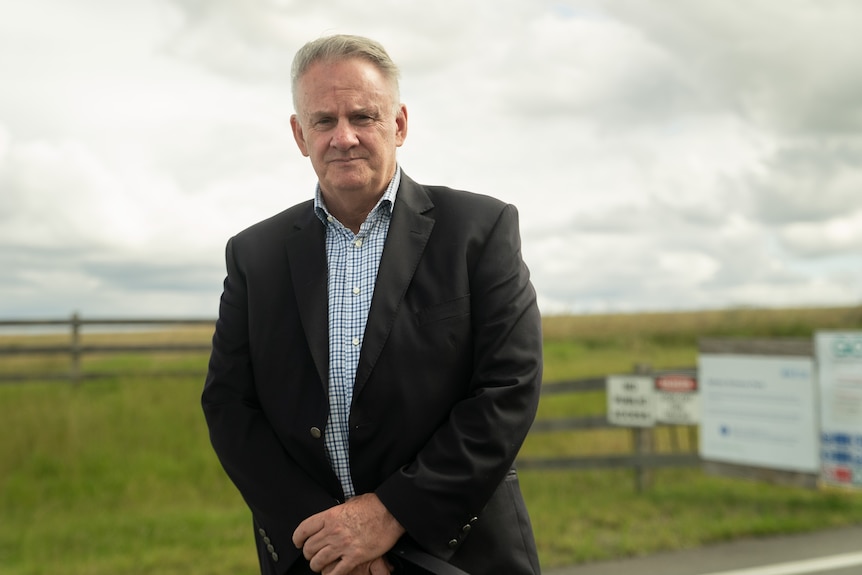 A man, standing near a field, with a concerned expression looks at the camera