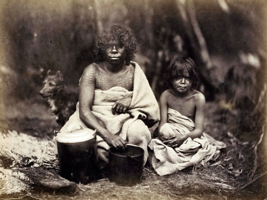 An historic photograph of mother and child wrapped in blankets cooking outdoors