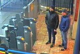 Two men in coats and beanies stand at train station gates.