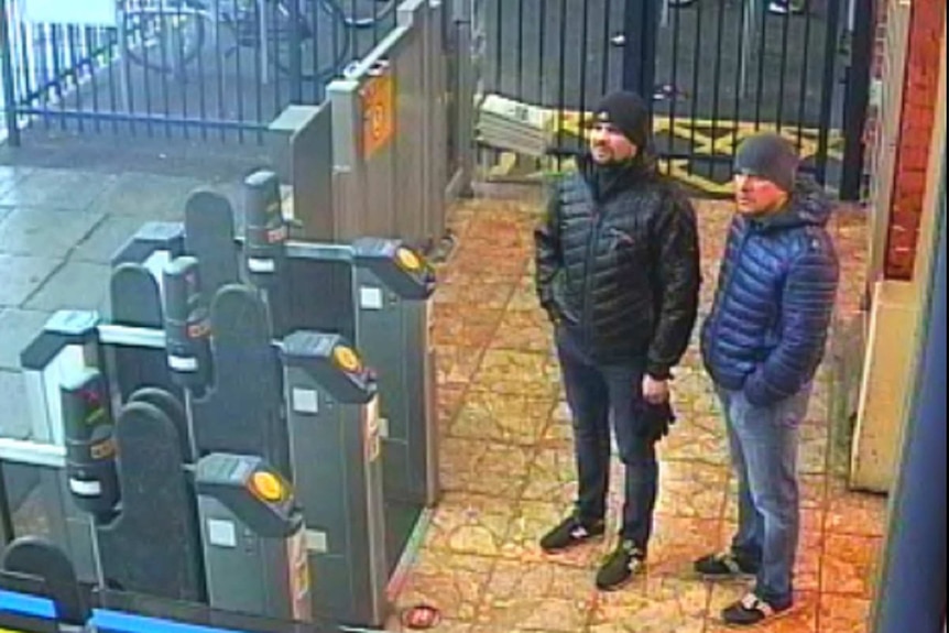 两个身穿大衣、头戴无檐小便帽的男子站在火车站门口。
