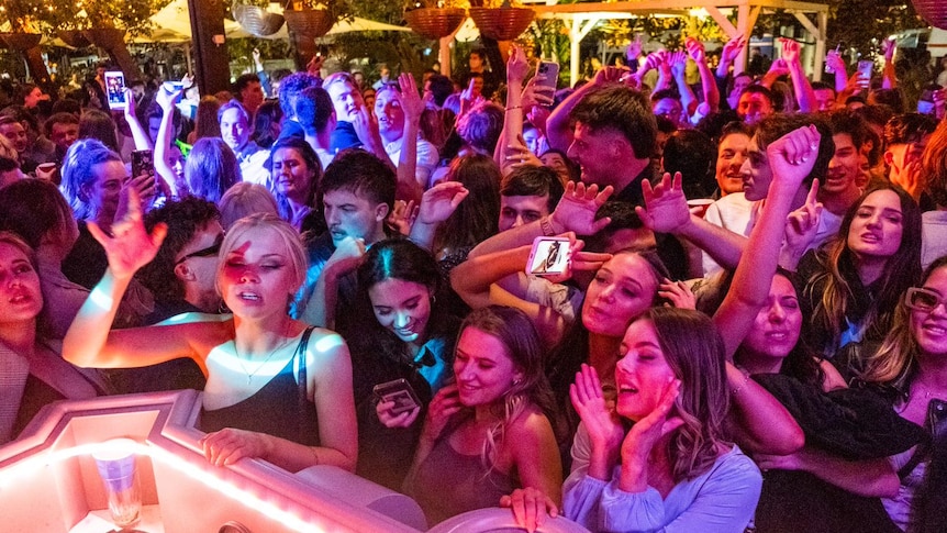 a group of young women and men stand in front a dj dancing