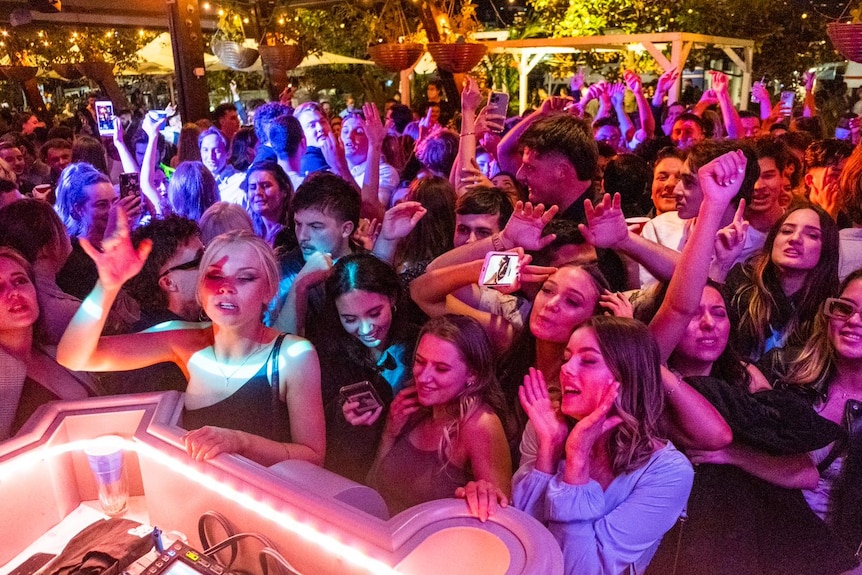 a group of young women and men stand in front a dj dancing