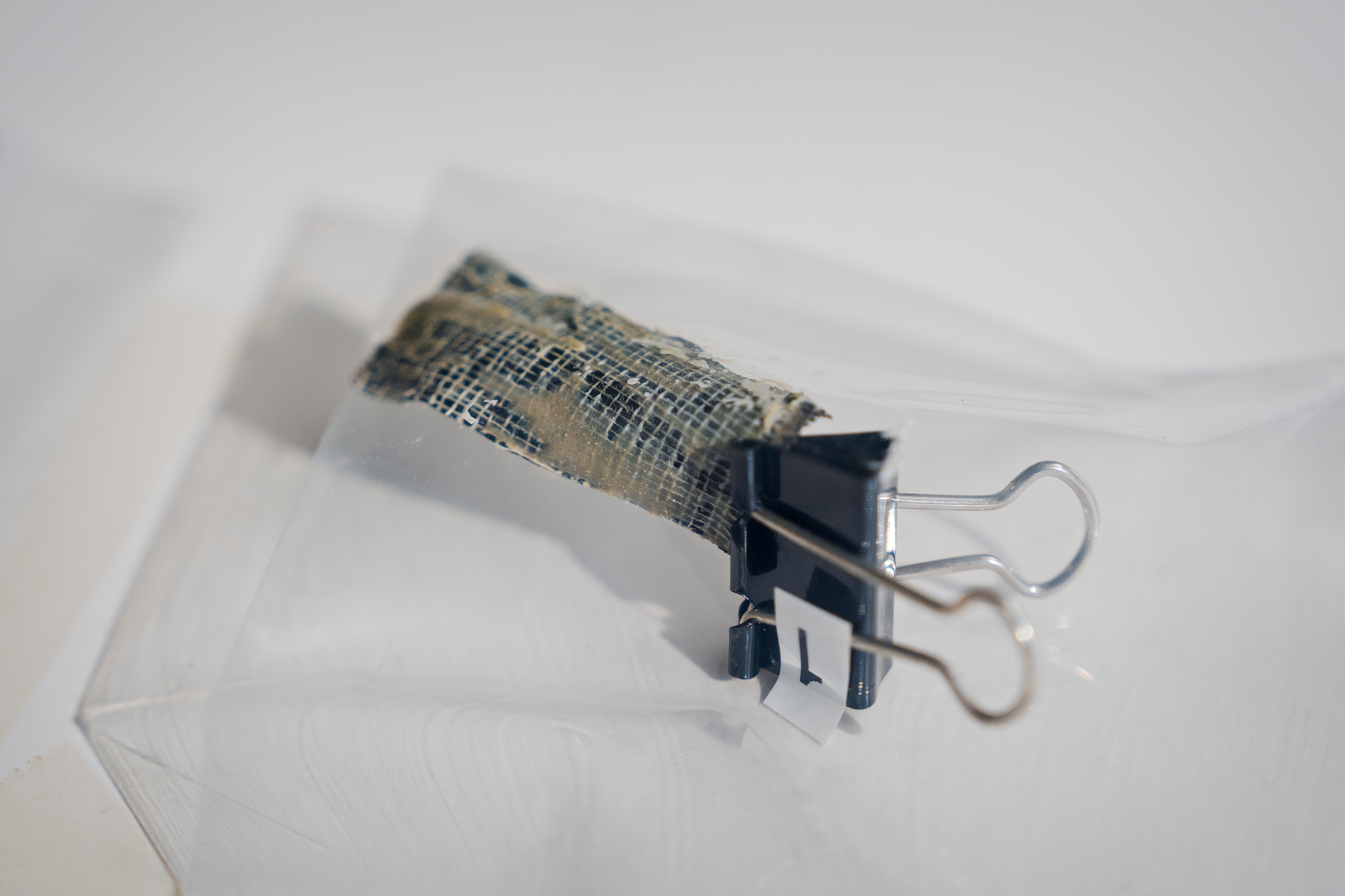 A close up shot of a piece of duct tape held with a black bull clip inside a clear evidence bag on a white table.