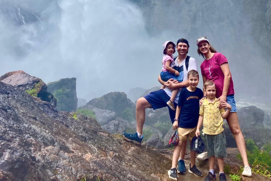 A young family stand at the base of a waterfall.